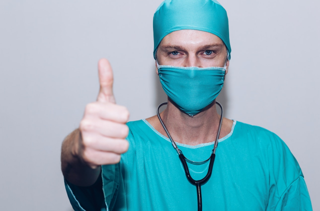 a doctor wearing a mask and looks forward to the camera pointing OK with the thumb